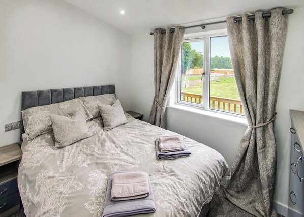 Un dormitorio con cama, cortinas, una ventana y vistas a un jardín.