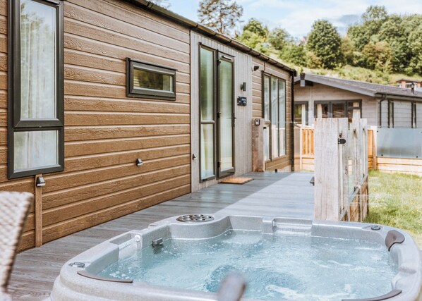 A wooden cabin with a hot tub, a covered porch, and a door leading to a covered area.