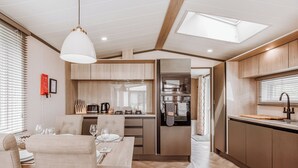 A modern kitchen with wooden cabinets, a dining area with a table and chairs, and a skylight above. - Sycamore Lodge VIP Hot Tub (Bridgnorth)