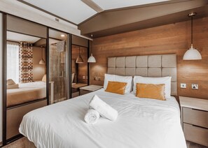 A hotel room with a large bed, a glass shower enclosure, and a wooden headboard.