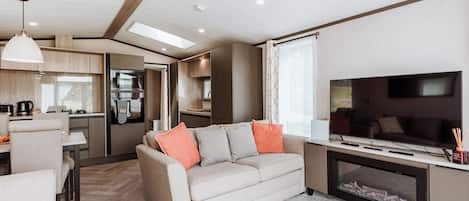 Interior moderno de una casa rodante con sala de estar, kitchenette y televisor.