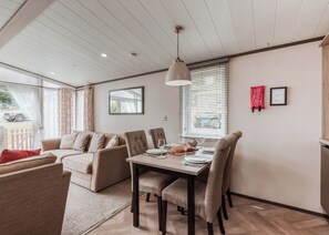 A modern room with a dining table, chairs, a sofa, and a large window with blinds.