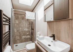 A modern bathroom with a glass shower enclosure, a white sink, and a wooden vanity.