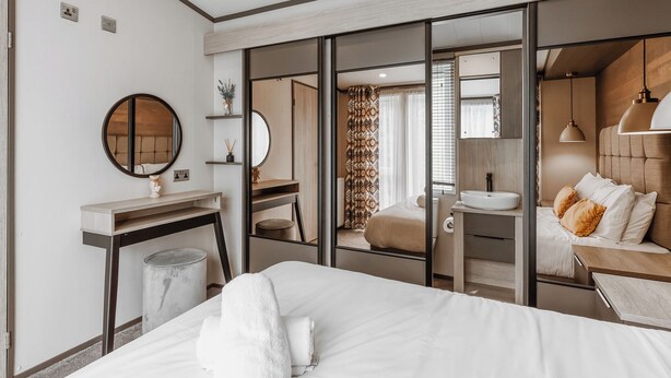 A modern hotel room with a bed, bedside table, mirror, and a view through a sliding door into a bathroom. - Sycamore Lodge VIP Hot Tub (Bridgnorth)