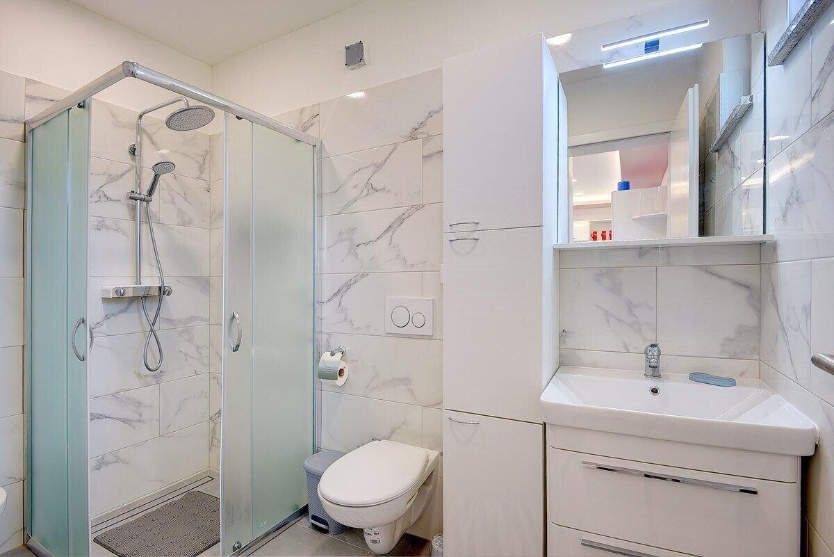 Une salle de bain moderne avec une douche à parois de verre, des toilettes blanches et un lavabo surmonté d’un miroir.