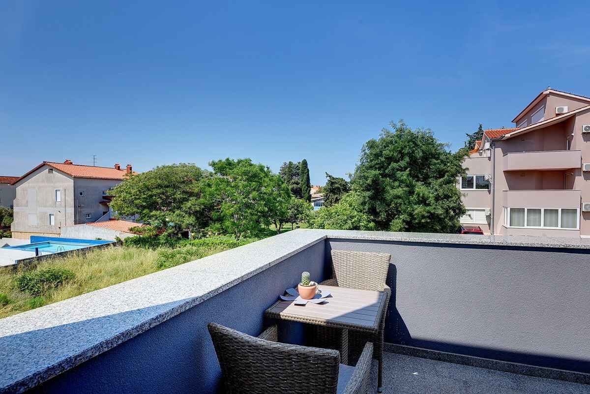 En tagterrasse med et bord og stole, en lille plantekasse og en swimmingpool i baggrunden.