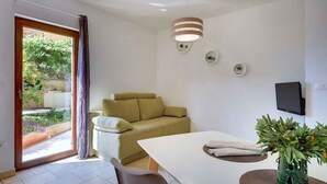 A modern living room with a sofa, a dining table, and a TV mounted on the wall. - Holiday apartment with a beautiful garden for shared use (Vinkuran)