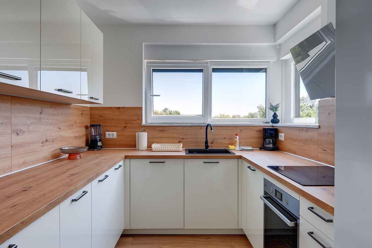 Una cocina moderna con armarios blancos, encimeras de madera, un lavamanos doble y un horno empotrado.