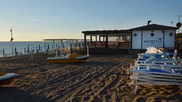 Ein am Strand gelegenes Gebäude namens "MOJITO" mit überdachter Sitzgelegenheit und Blick auf das Meer.