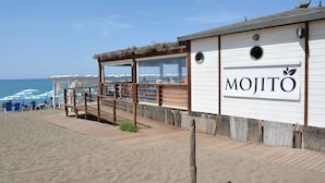 Um restaurante à beira-mar chamado "MOJITO", com um deque de madeira e telhado de palha.