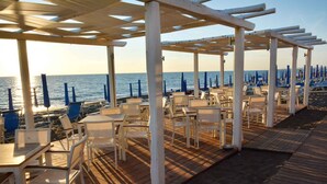 Um restaurante à beira-mar com mesas e cadeiras ao ar livre e um deque de madeira que dá para a praia.