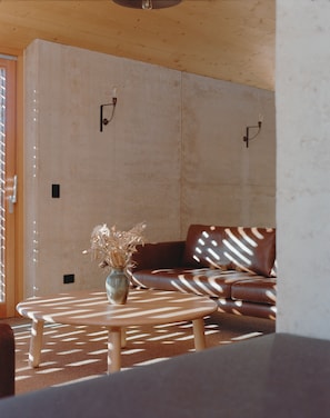 A modern living room with a brown leather sofa, a wooden coffee table, and a vase with dried flowers.