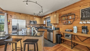 Una cocina moderna con armarios de madera, una isla central con taburetes, un rincón para café y un letrero de pizarra.