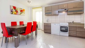 Eine moderne Küche mit weißen Schränken, einem eingebauten Backofen und einem Essbereich mit einem roten Tisch und Stühlen.
