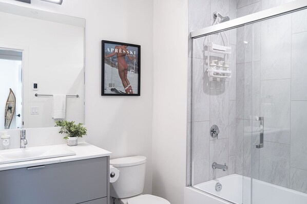 Een moderne badkamer met een douche met glazen wand, een wit wastafelmeubel en een toilet.
