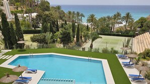 A rectangular swimming pool with a diving board, surrounded by blue lounge chairs and thatched umbrellas.
