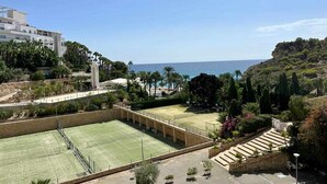 A tennis court with a view of the sea and a building in the background.
