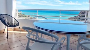 A balcony with a round table and chairs, a view of the ocean, and a chair with a unique design.