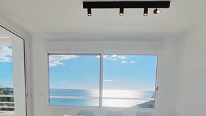 A dining area with a table and chairs, large windows with a view of the sea, and a ceiling light fixture.