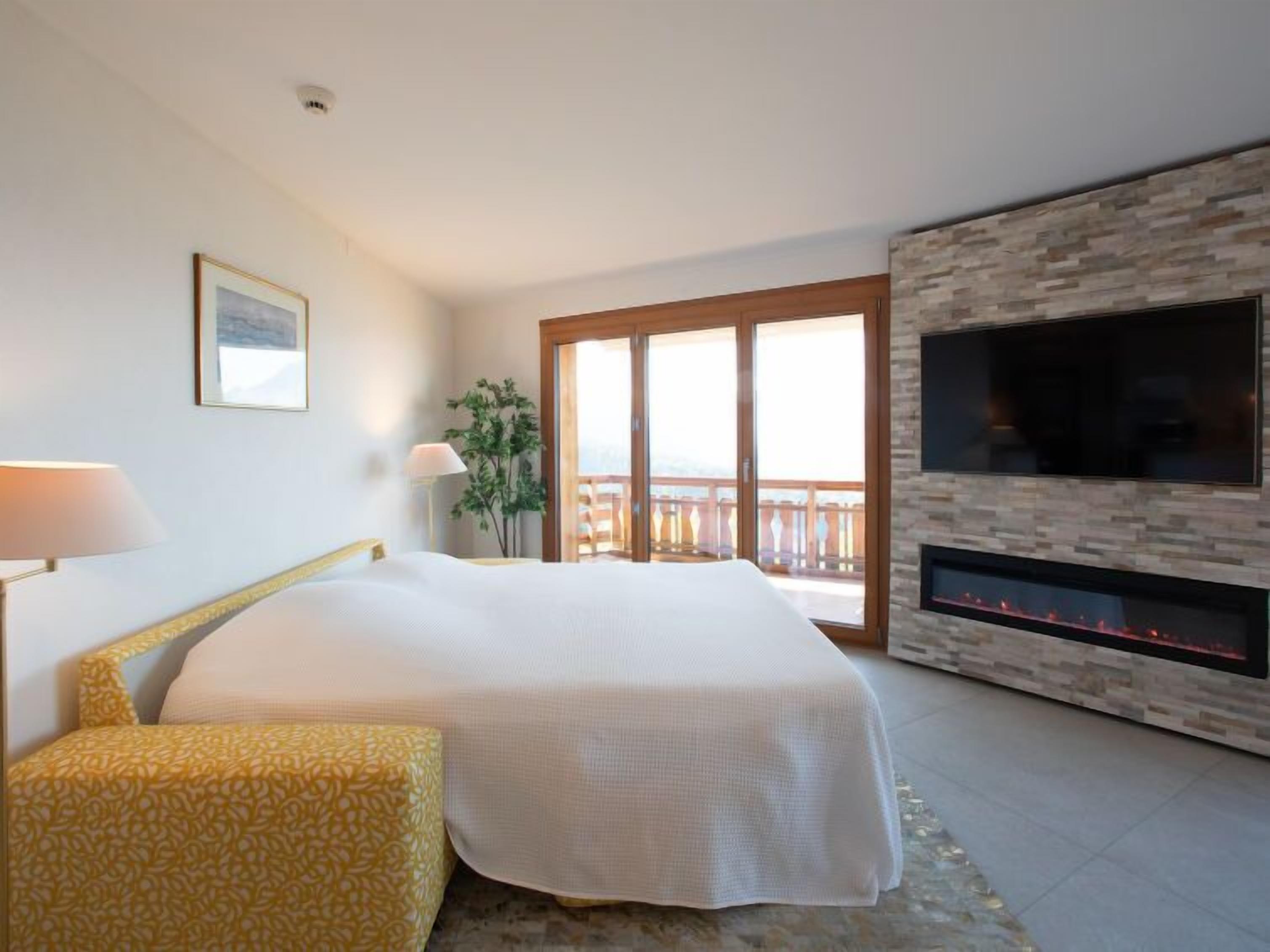 Ein Hotelzimmer mit Bett, Fernseher, Kamin und Balkon mit Aussicht.