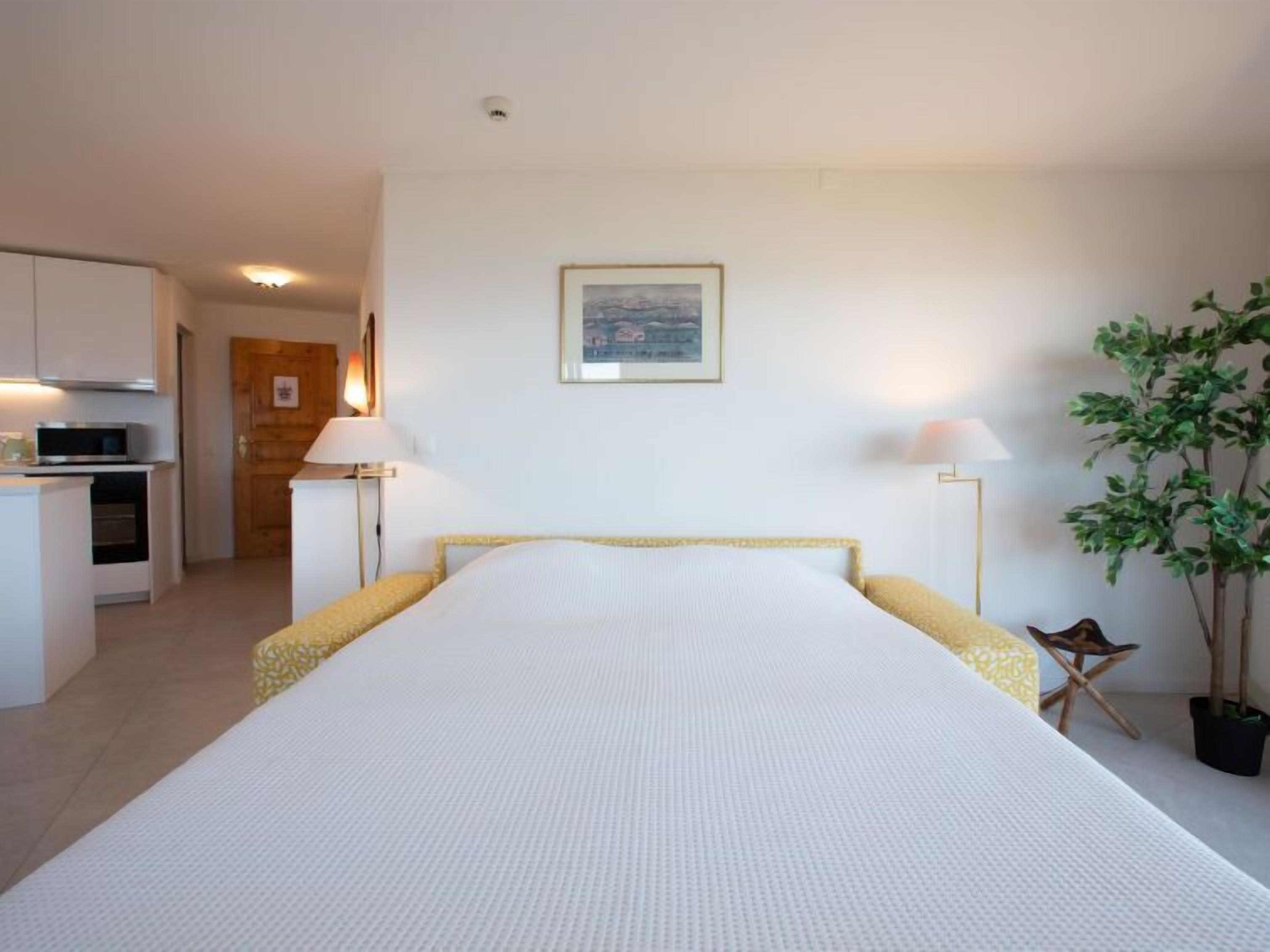 Une chambre à coucher avec un lit, des lampes de chevet, une plante en pot et un tableau encadré au mur.