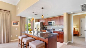 A modern kitchen with a central island, wooden cabinets, stainless steel appliances, and a large window. - Maui Resort Rentals: Honua Kai - 4 Total Bedrooms, Ground Floor Interior Courtyard, Steps to Pools, Beach, BBQs! (Lahaina)