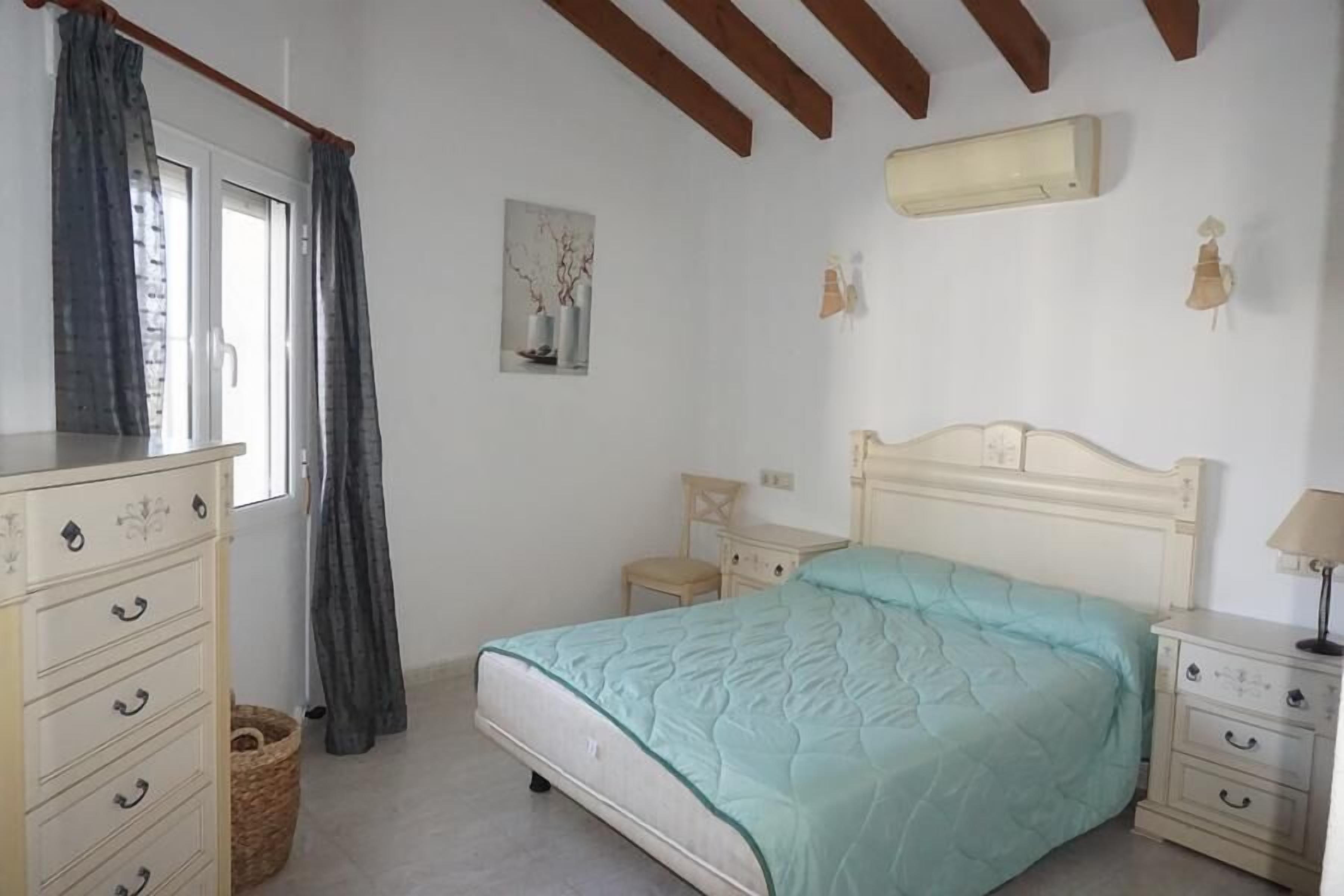 Une chambre à coucher avec un lit, une commode, une table de chevet et une fenêtre avec des rideaux.