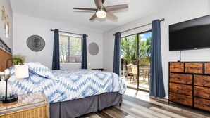 Un dormitorio con cama, ventilador de techo, televisión, cómoda y ventana con cortinas.