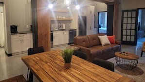 A modern kitchen with white cabinets, a dining table with a potted plant, and a brown leather sofa with a red pillow. - Welcome to the Aurora (Duluth)