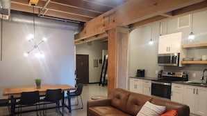 A modern living room with a brown leather sofa, a wooden dining table with chairs, a round coffee table, and a kitchen area with white cabinets and appliances. - Welcome to the Aurora (Duluth)
