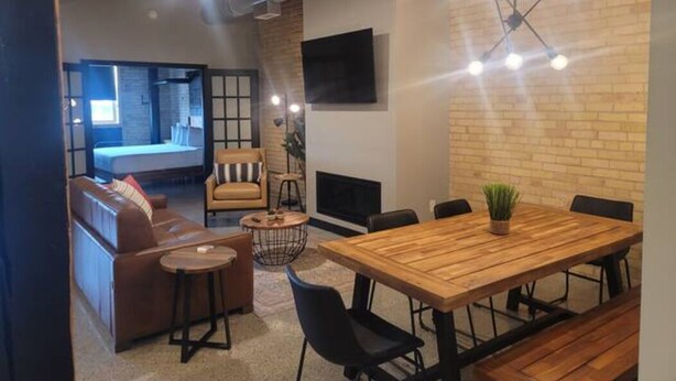 A modern interior with a wooden dining table, black chairs, a brown leather sofa, and a small round table with a plant. - Welcome to the Aurora (Duluth)