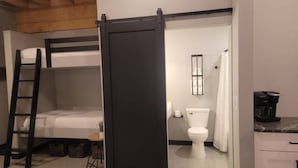 A compact room with a bunk bed, a small table with a plant, a toilet, and a kitchen area with a coffee maker. - Welcome to the Aurora (Duluth)