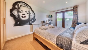 Ein Schlafzimmer mit einem großen Bett, Wandbild, Fernseher, einem Fenster mit Vorhängen und einer Heizung.