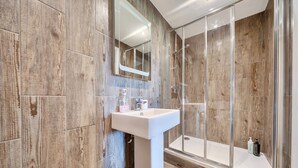 Ein Badezimmer mit Holzwand, Waschbecken in Weiß und einer Duschkabine aus Glas.