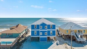 Propiedad frente a la playa con un edificio grande azul, un edificio amarillo más pequeño y un área de piscina.