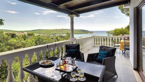 A balcony with wicker furniture, a table set with glasses and a tray of food, and a scenic view of the sea and hills. - Villa with pool and sea view (Banjole)