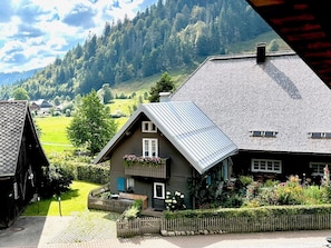 Een traditionele chalet met een schuin dak, een houten omheining en een tuin met bloemen en struiken.