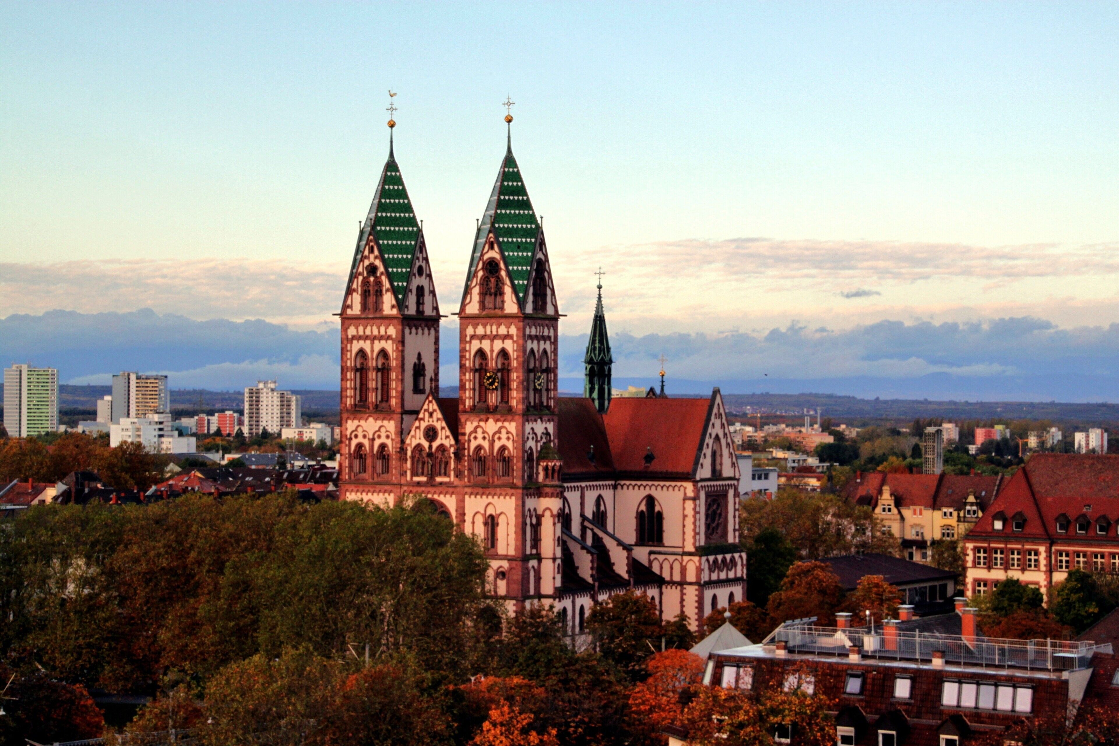 Eine historische Kirche mit zwei Türmen, umgeben von städtischen Gebäuden und Bäumen.