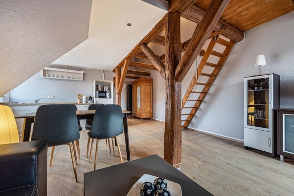 A modern kitchen with a dining area, wooden beams, and a staircase.
