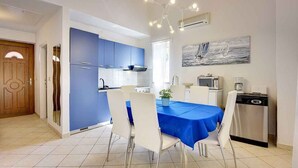 A modern kitchen with blue cabinets, a dining table with white chairs, and a painting on the wall. - Villa with pool near the beach (Banjole)