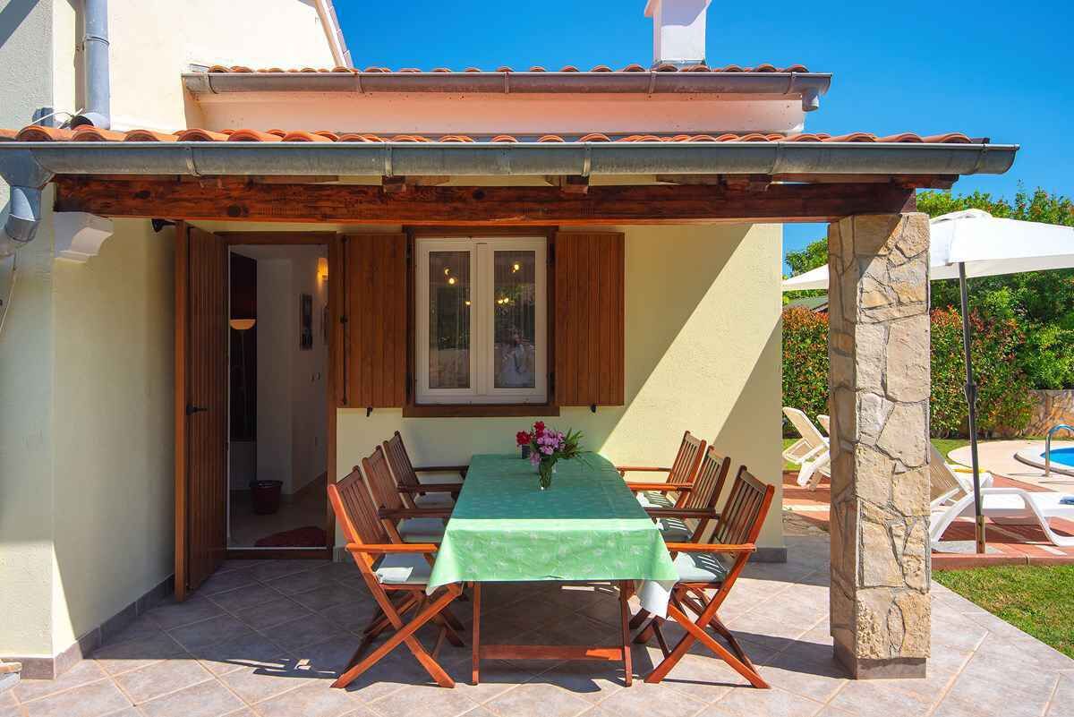 En udendørs spiseplads med bord og stole, et pergola og udsigt til en swimmingpool.