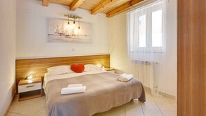 A bedroom with a wooden ceiling, a bed with a beige bedspread, a red pillow, and a painting of sailboats on the wall. - Villa with pool near the beach (Banjole)