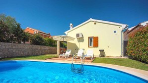 A swimming pool with a stone wall, a small building with a window and a door, and a chair under an umbrella. - Villa with pool near the beach (Banjole)