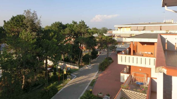 Un edificio a più piani con un viale rosso, alberi e cielo sereno.