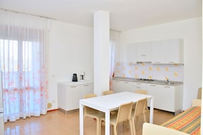 A compact kitchen with white cabinets, a dining table with chairs, and a small coffee station.