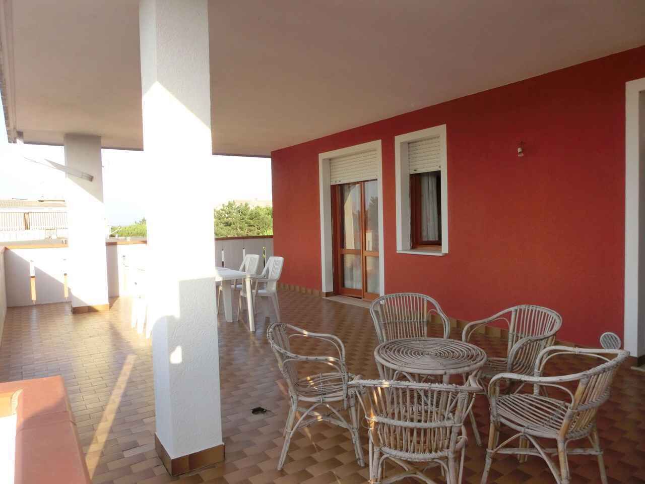 A covered outdoor patio with wicker furniture, a white table, and a red wall.