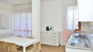Una cucina con un piano cottura, un lavello e pensili, un tavolo da pranzo con sedie e tende floreali.