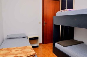 A dormitory room with bunk beds, a wooden wardrobe, and a small desk.