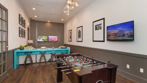 A room with a foosball table, a bar area with stools, and a TV mounted on the wall. - Serene Escape in the Pines- shopping, dining, entertainment-Iron Man (Spring)