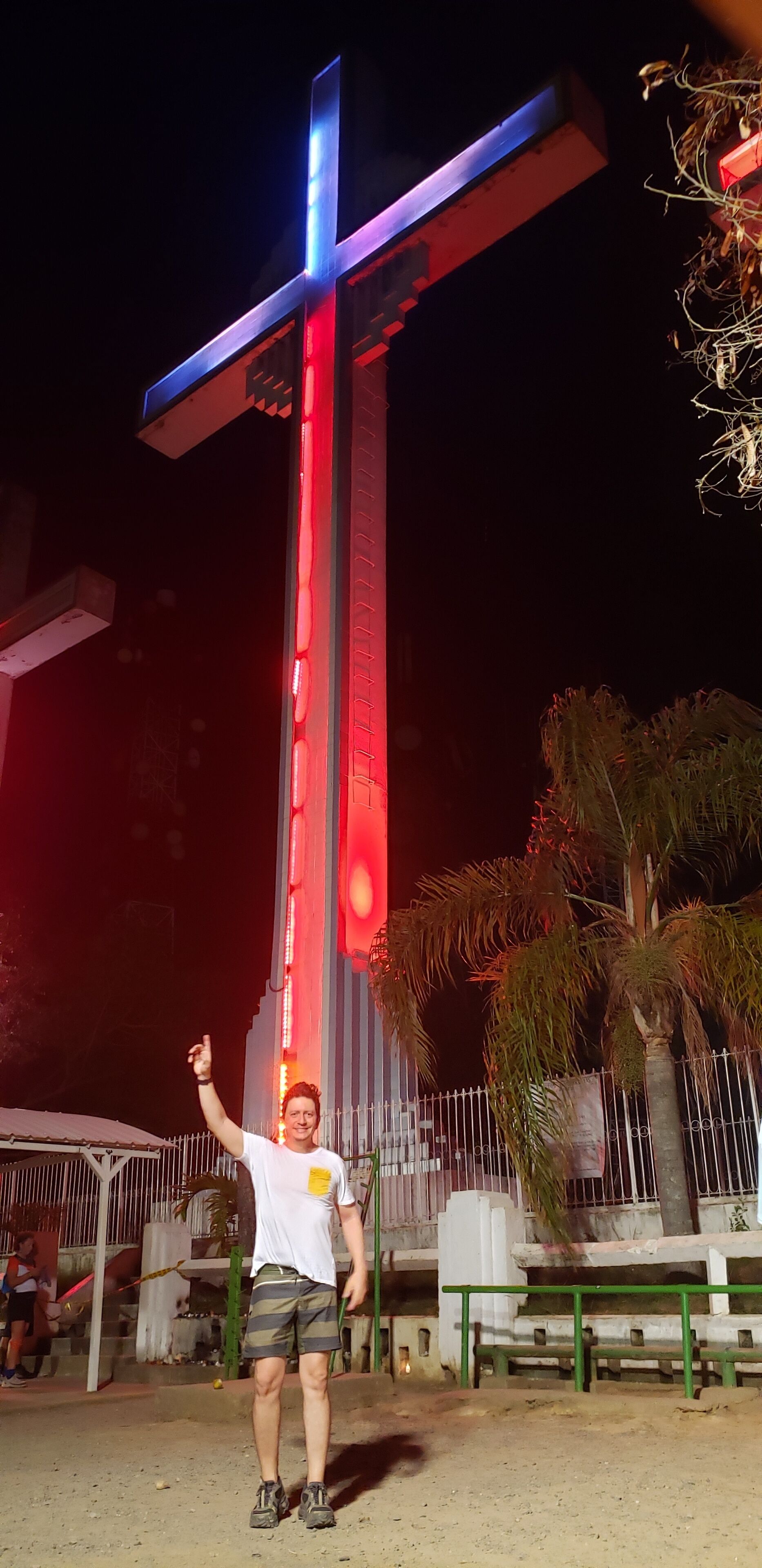 A person standing in front of a large illuminated cross structure at night.